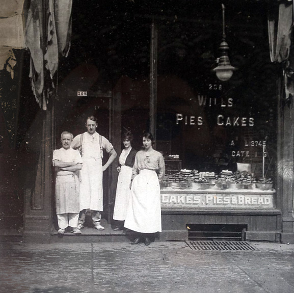 Previous residents of 208 Queen St West standing outside the building. Window reads "Wills Cakes, Pies & Bread".